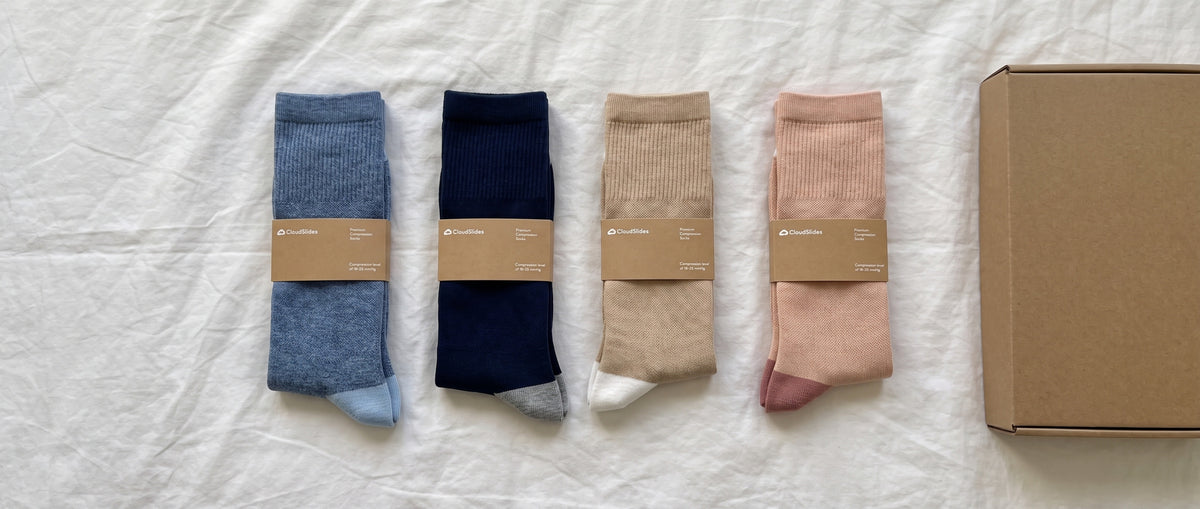 Four pairs of compression socks in different everyday colors laid flat next to their packaging